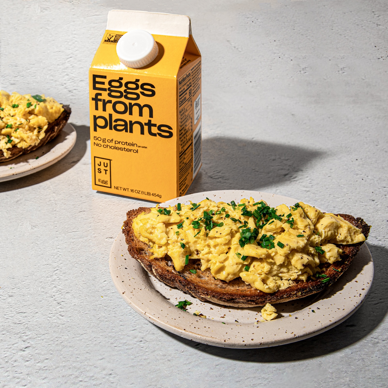 a photo of a carton of a vegan egg substitute next to a plate of scrambled (vegan) eggs on a piece of toast